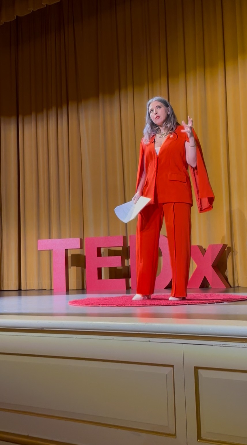 Sandy speaking on a TEDx stage in a bold red suit - dynamic and real